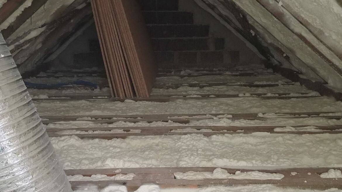 Poddasze w Żłobku w trakcie ocieplania: biała pianka izolacyjna wypełnia przestrzeń między krokwiami, widoczne deski stropowe, rura wentylacyjna i płyty kartonowo-gipsowe przygotowane do montażu.