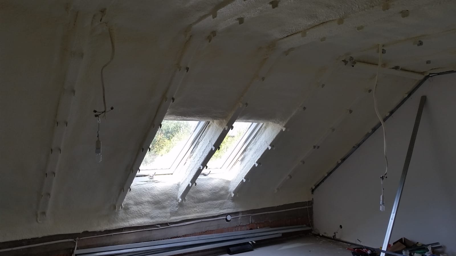 Ocieplone pianką PUR poddasze z widocznymi oknami dachowymi, niezabezpieczonymi przewodami elektrycznymi i metalowymi profilami przy ścianie.