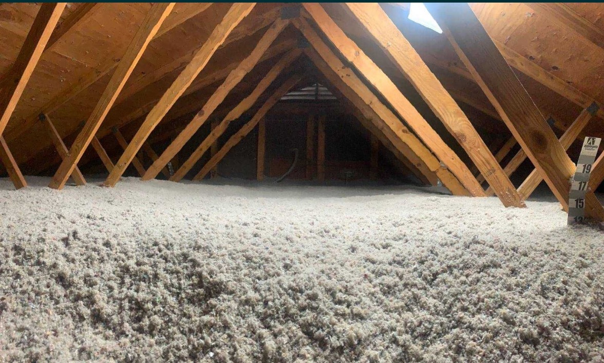 Poddasze z drewnianą konstrukcją krokwiową wypełnione warstwą izolacyjną z wełny mineralnej, widoczna skala pomiarowa grubości izolacji.