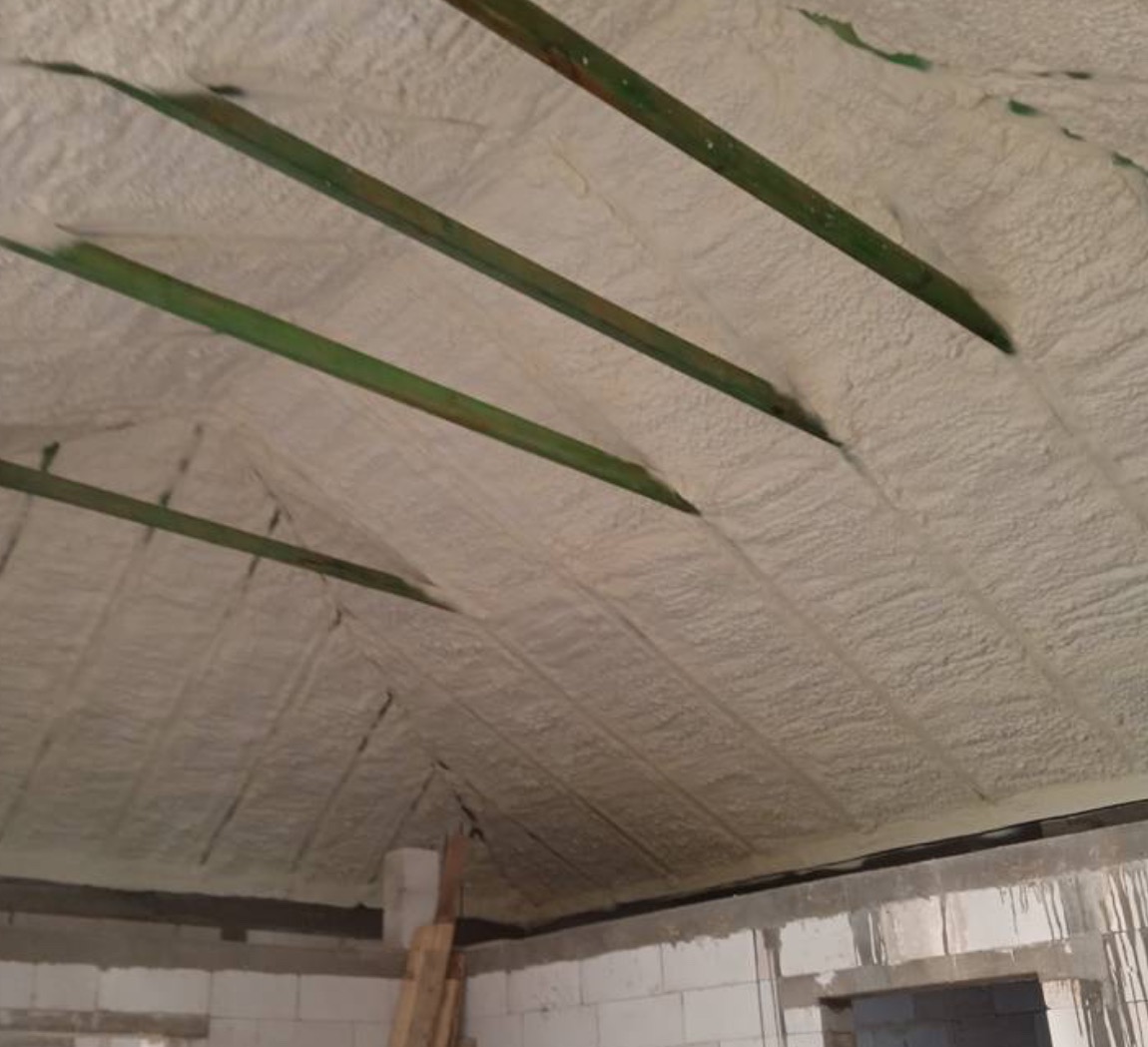 Poddasze pokryte warstwą izolacyjną z pianki, widoczne drewniane belki stropowe, surowy stan wykończenia ścian z bloczków.