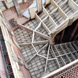 Wysoki kąt widzenia na konstrukcję zbrojeniową i drewniane szalunki przygotowane do wylewania stropu, z widoczną częścią murowanej ściany z pustaków ceramicznych.