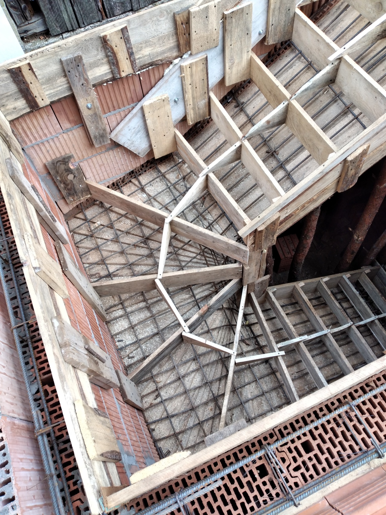 Wysoki kąt widzenia na konstrukcję zbrojeniową i drewniane szalunki przygotowane do wylewania stropu, z widoczną częścią murowanej ściany z pustaków ceramicznych.