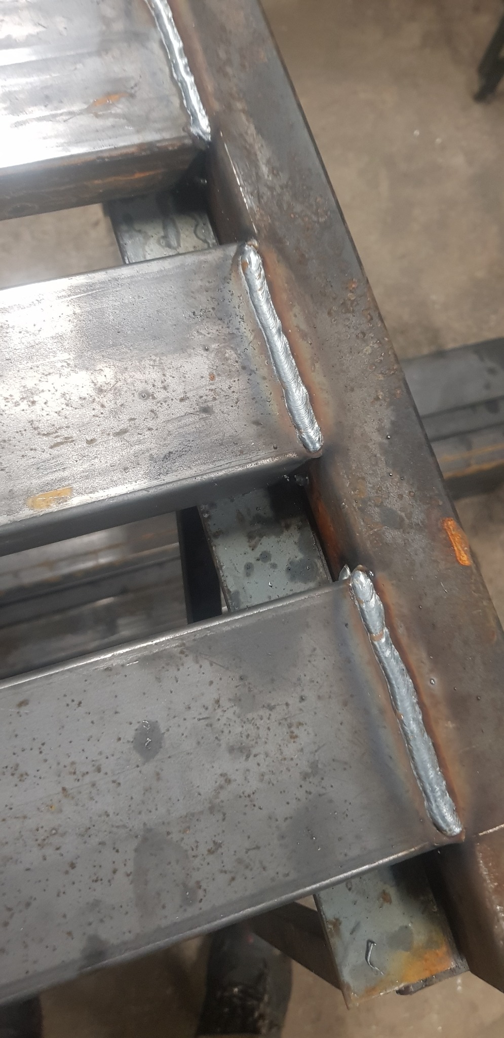 Spoina łącząca stalowe profile pod kątem prostym, widoczne ślady po spawaniu na szarym metalu, surowe wykończenie.