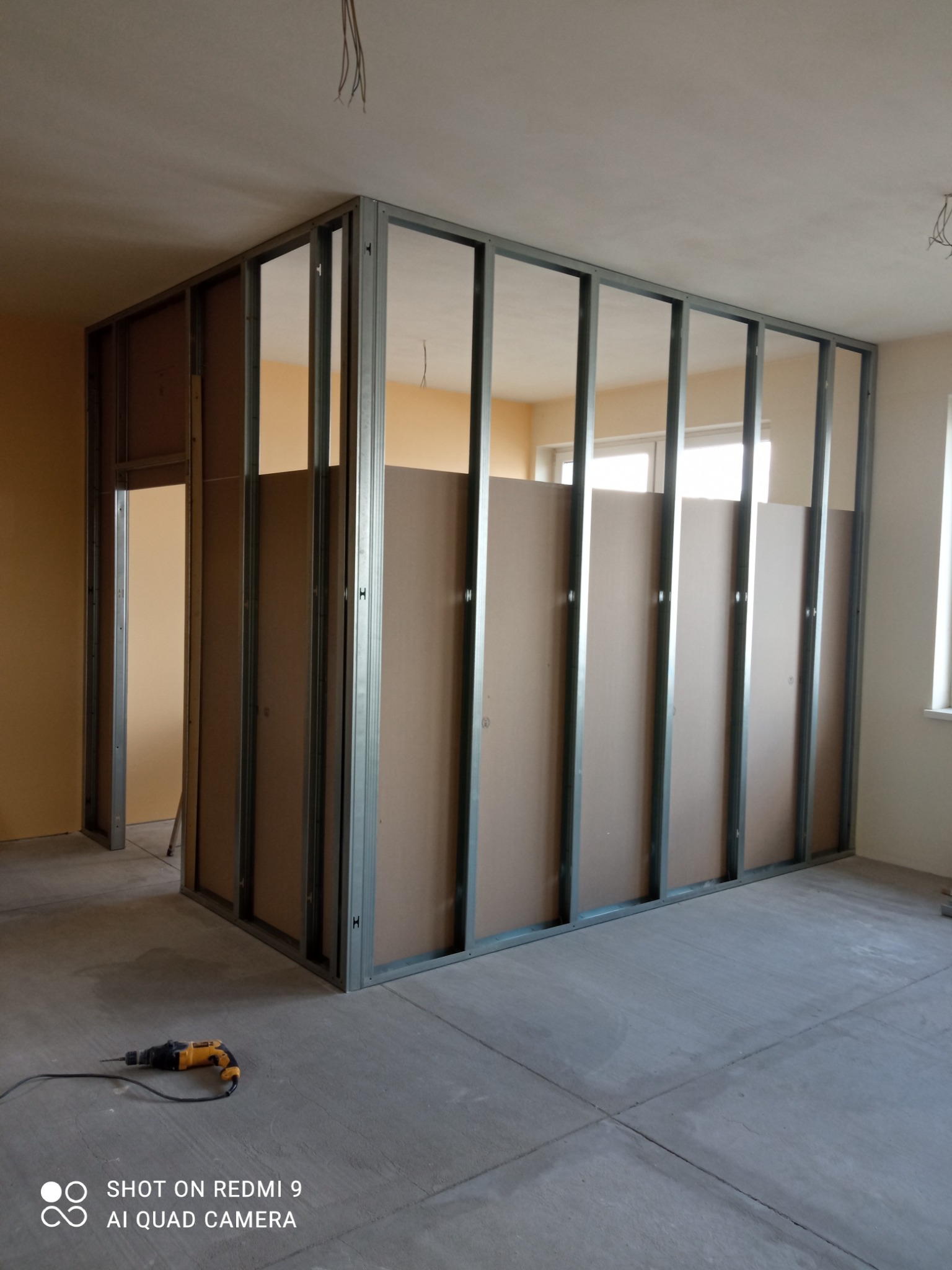 Stelaż z profili metalowych do ścian działowych z płyt kartonowo-gipsowych w trakcie montażu; widoczna wiertarka na podłodze.