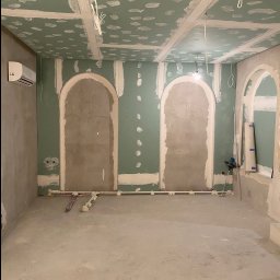 Wykończenia z klimatem - Pokój w trakcie prac wykończeniowych: ściany obłożone zielonymi płytami gipsowo-kartonowymi, widoczne szpachlowane łączenia, przygotowane łukowe wnęki, wystające przewody elektryczne i rury...