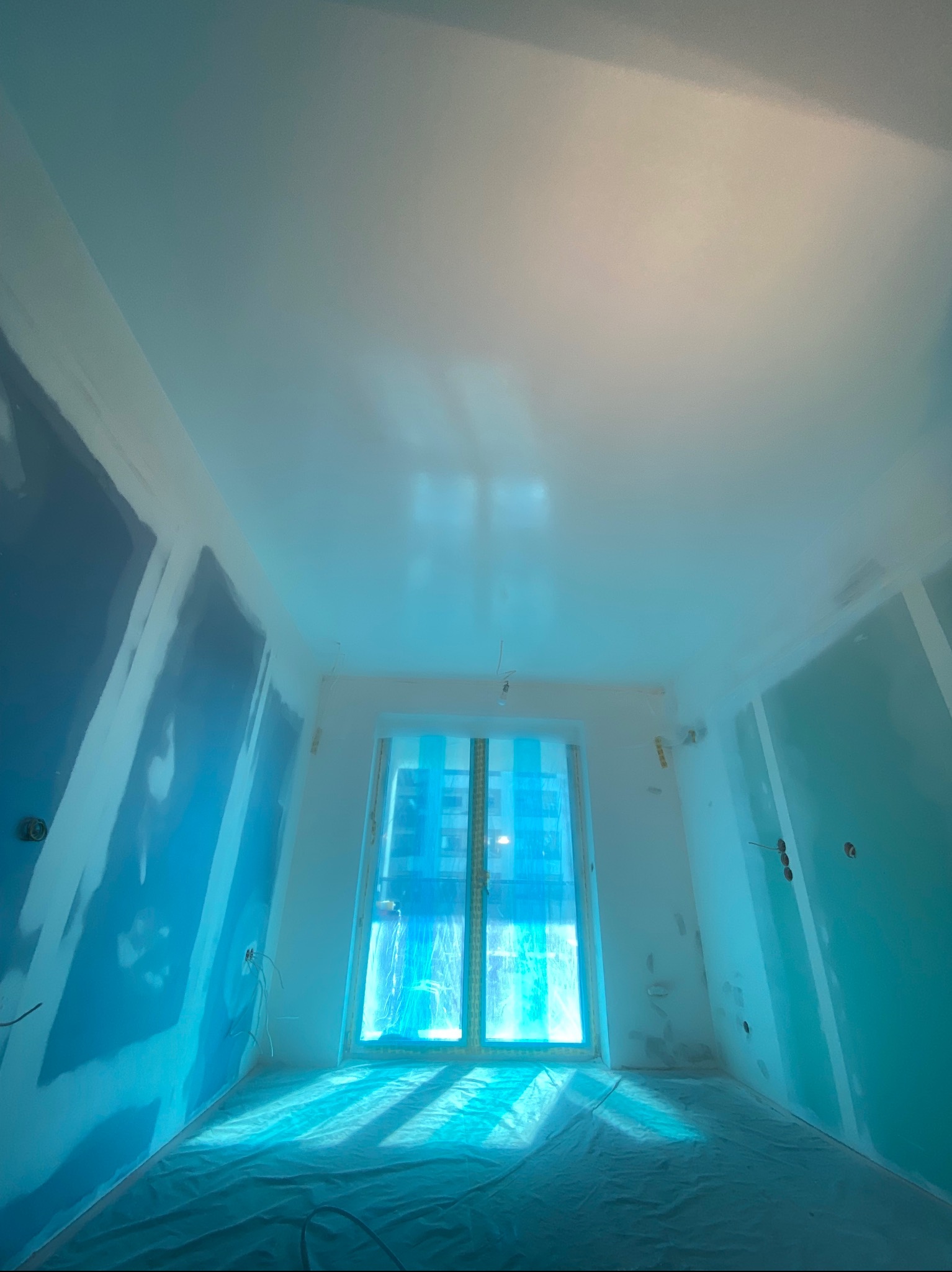 Pokój w trakcie prac wykończeniowych: ściany z płyt kartonowo-gipsowych, zabezpieczona folią podłoga, widoczne kable elektryczne wystające ze ściany.