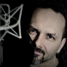 Mocny Głos Jerzy Janik - Portret mężczyzny w studiu nagrań w Krakowie, z mikrofonem studyjnym i wygłuszeniem akustycznym w tle. Ciemne oświetlenie, skupienie na twarzy lektora.