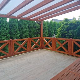 EcoTaras - Zadaszony taras z drewnianą pergolą i balustradą krzyżową, wyłożony płytkami imitującymi drewno. W tle wysokie tuje.