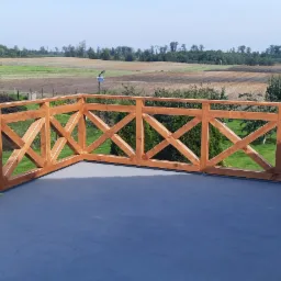 Drewniana balustrada z krzyżowym wzorem na tarasie z widokiem na pola i drzewa w oddali, na podłodze tarasu leży niebieska plandeka