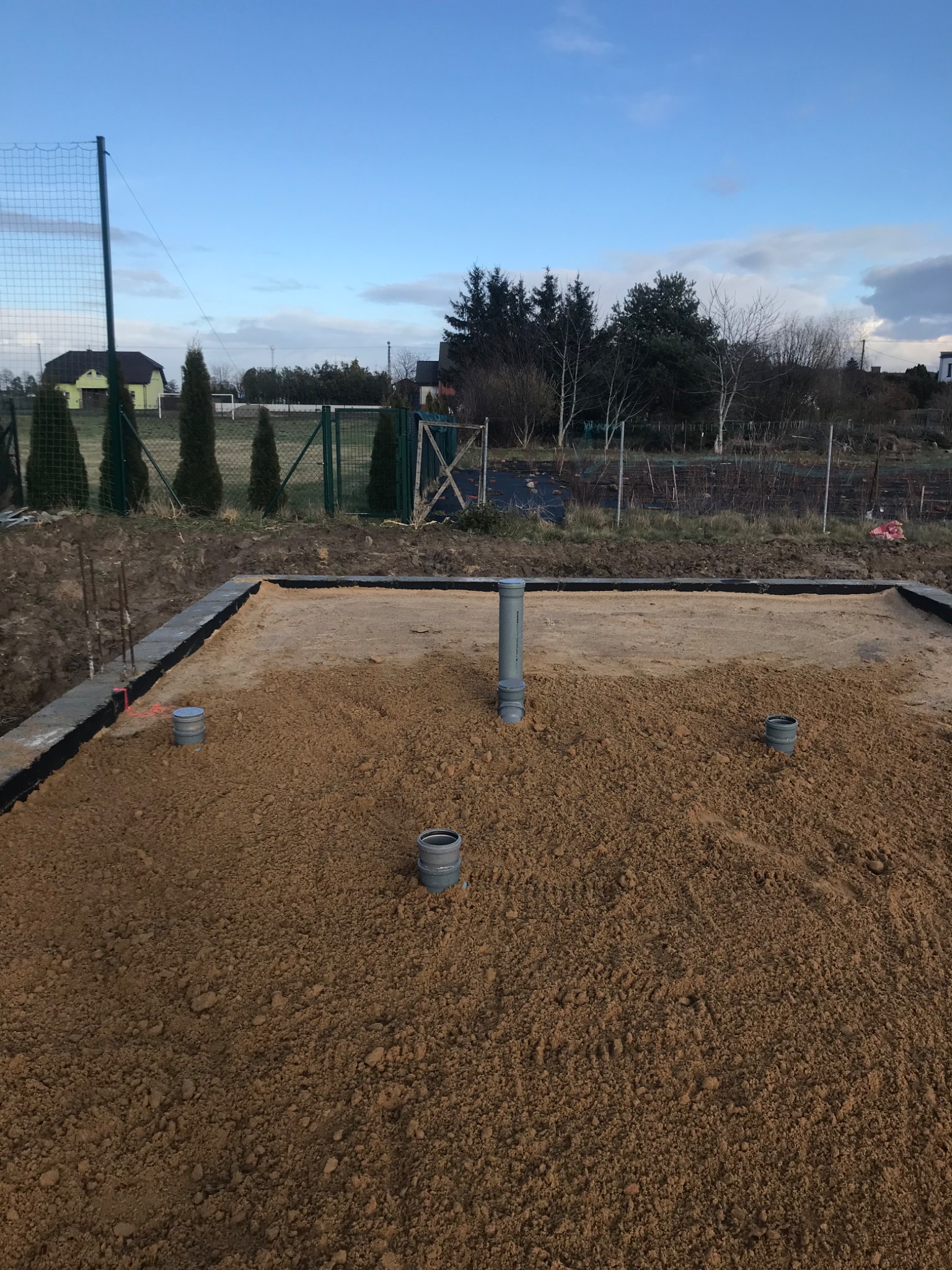 Przygotowany fundament pod budowę z wyprowadzonymi pionami kanalizacyjnymi, podsypany piaskiem, widok z góry na działkę.