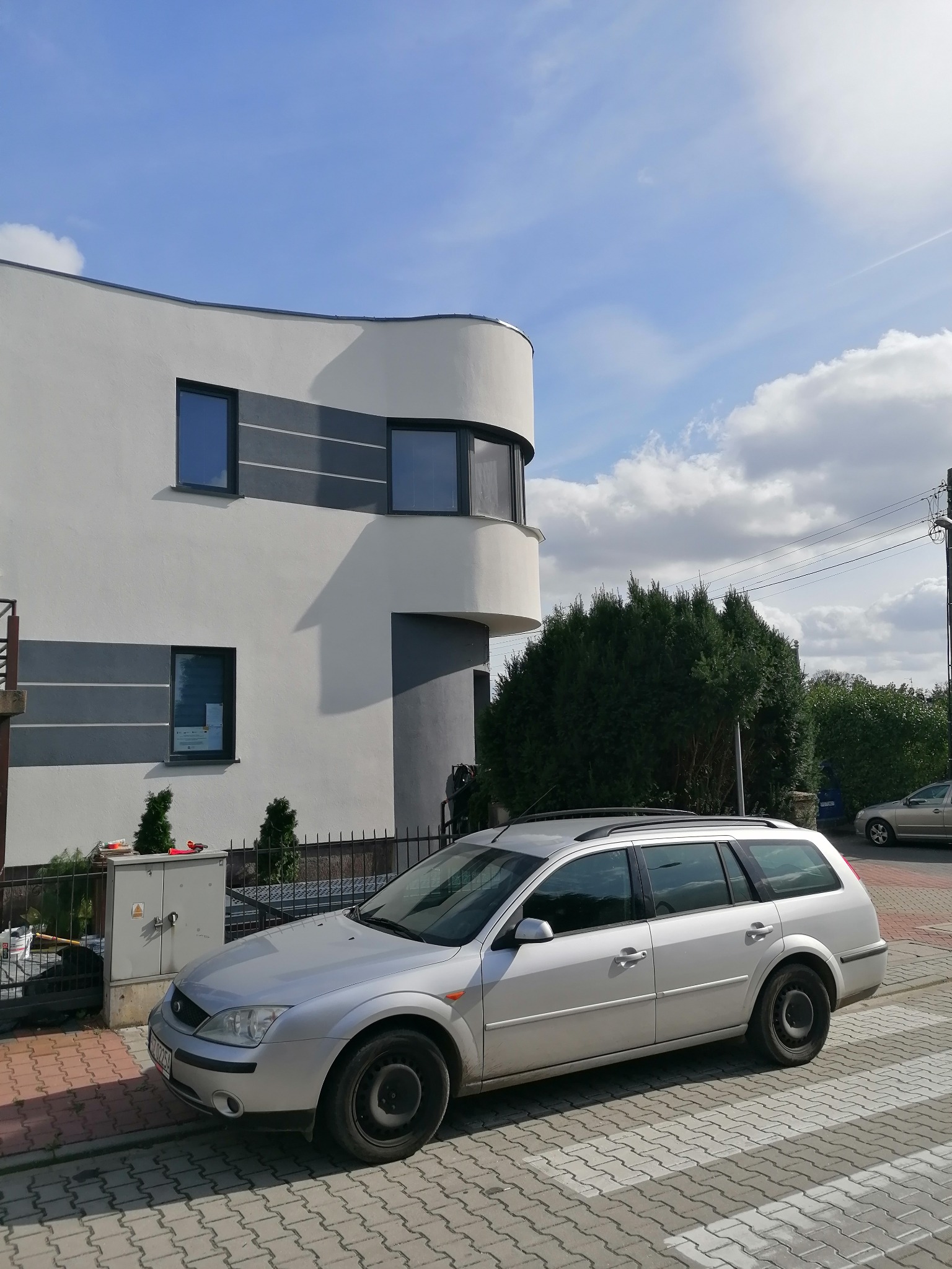 Nowoczesny dom jednorodzinny z elementami w kolorze szarym, widoczny z zewnątrz, z zaparkowanym srebrnym kombi na pierwszym planie.