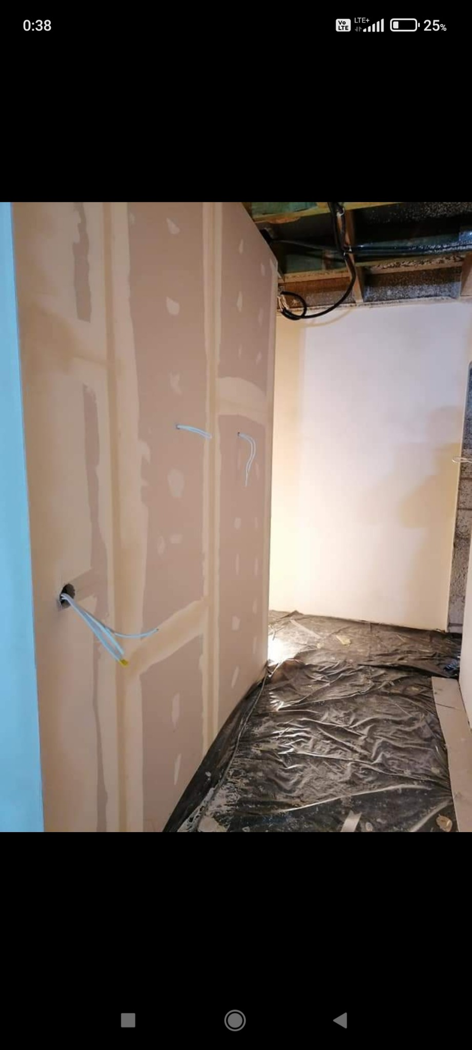 Ściana z płyt gipsowo-kartonowych po nałożeniu gładzi szpachlowej, widoczne przewody elektryczne wychodzące z otworu, podłoga zabezpieczona folią ochronną.