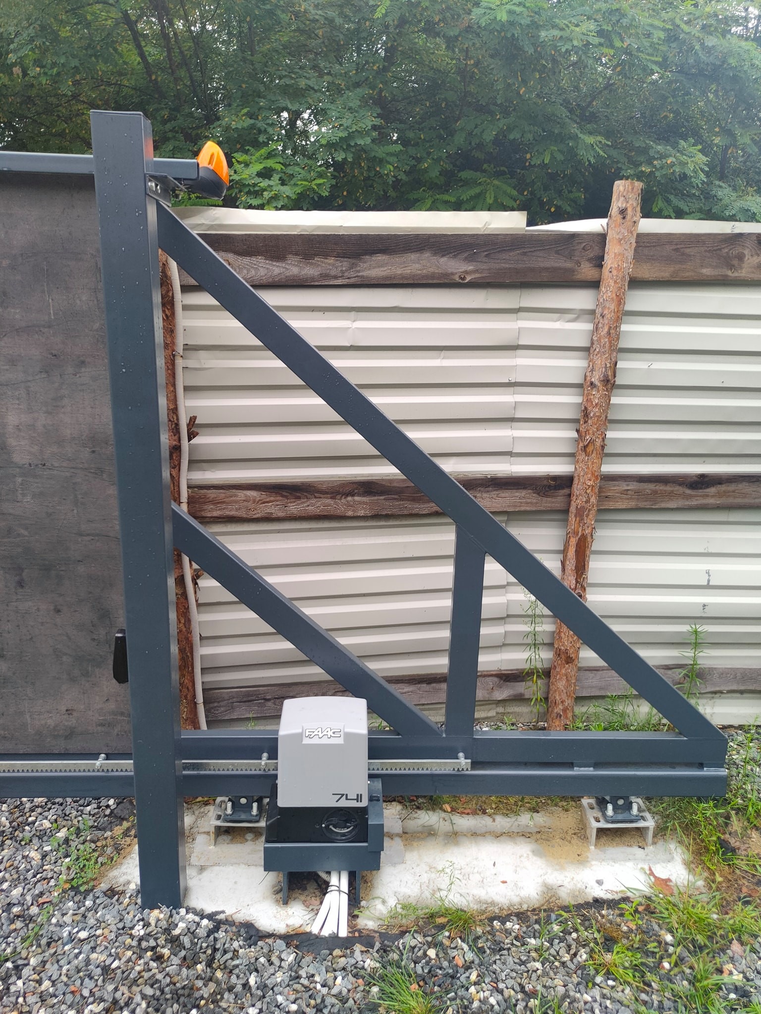 Szara przesuwna brama z zamontowanym napędem FAAC 741, widoczna lampa ostrzegawcza i fragment ogrodzenia z blachy trapezowej.