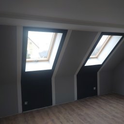 Maciej Szczęsny - Poddasze z dwoma oknami dachowymi po malowaniu ścian na szaro i czarno z panelami podłogowymi o wzorze drewna.
