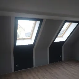 Poddasze z dwoma oknami dachowymi po malowaniu ścian na szaro i czarno z panelami podłogowymi o wzorze drewna.