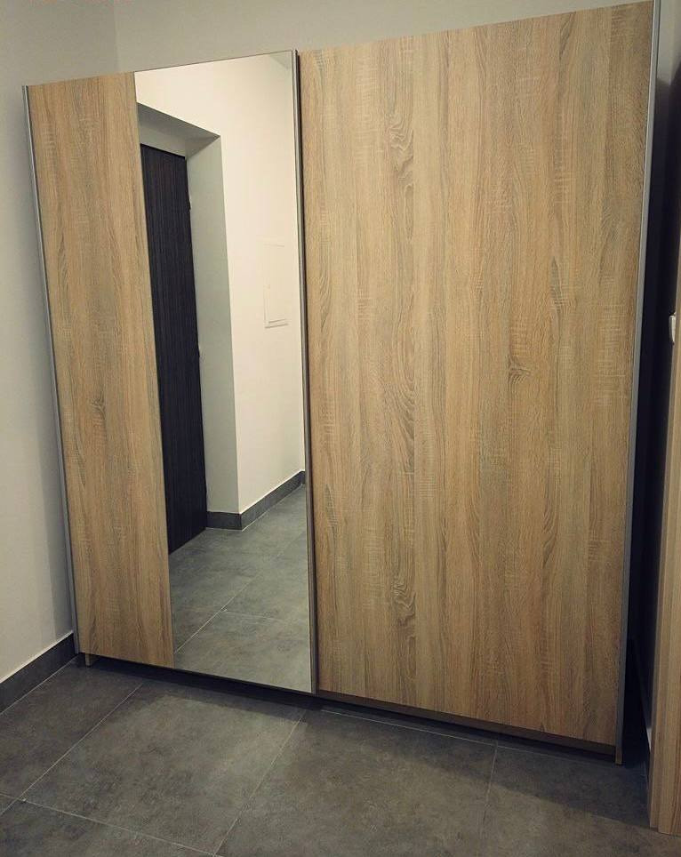 Szafa przesuwna z lustrem i drewnopodobnym wykończeniem, widoczne szare płytki podłogowe i fragment ściany z drzwiami w tle.