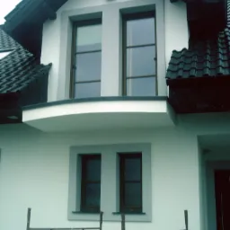 Elewacja domu z dwoma oknami na górze i dwoma na dole, jasna ściana, ciemna dachówka, widoczne rusztowanie w dolnej części kadru.