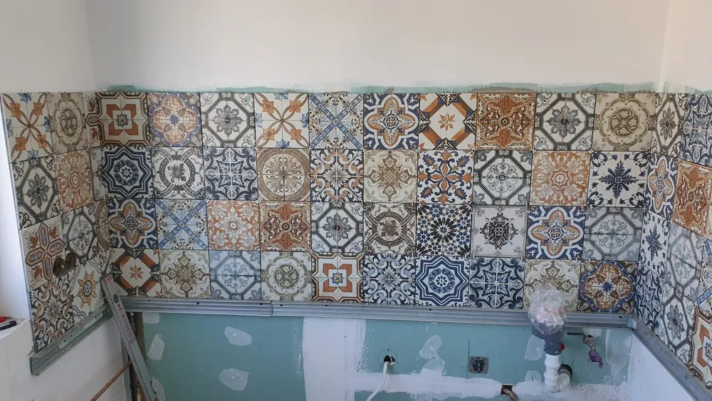 Ściana z ułożonymi dekoracyjnymi płytkami ceramicznymi w stylu marokańskim, widoczne niedokończone prace instalacyjne i fragment ściany z zieloną płytą gipsowo-kartonową.