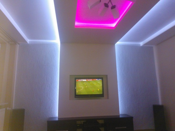 Pokój z dekoracyjnym oświetleniem LED w suficie i ścianach, centralnie umieszczony telewizor w zabudowie.