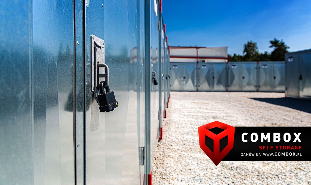 Szereg zewnętrznych, metalowych boksów do przechowywania, z czarną kłódką zabezpieczającą jeden z nich, na żwirowym podłożu i pod błękitnym niebem.