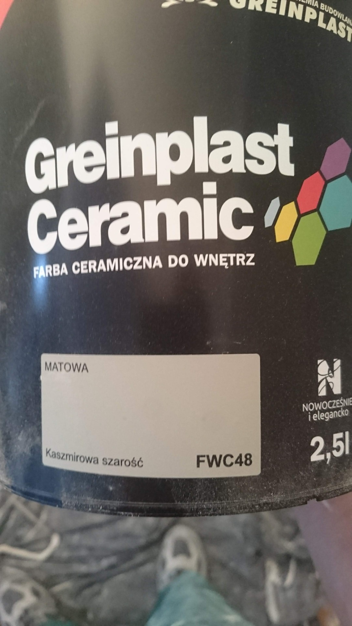 Puszka czarnej, matowej farby ceramicznej Greinplast w odcieniu 'Kaszmirowa szarość' FWC48, 2,5l, z widocznym fragmentem podłogi i buta w tle.