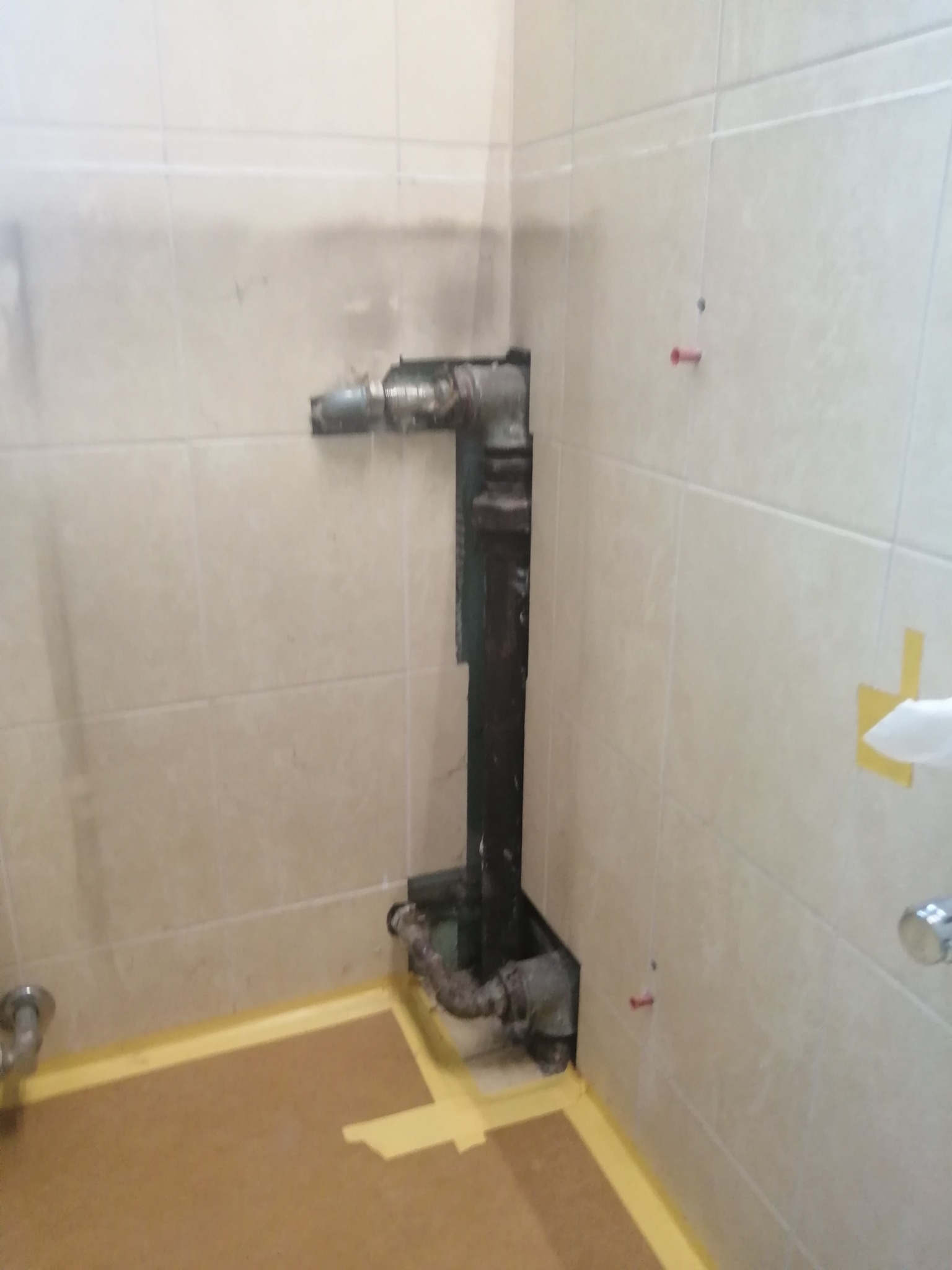 Fragment łazienki w trakcie remontu z widocznymi rurami kanalizacyjnymi, zabezpieczoną podłogą i fragmentami płytek.