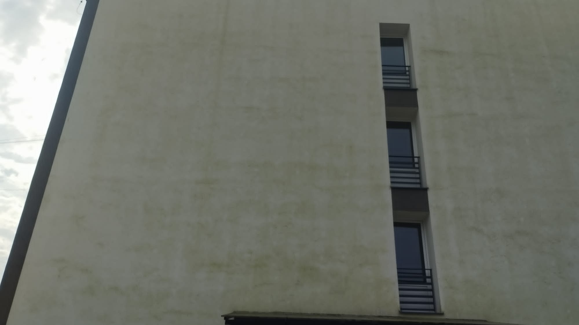 Elewacja budynku wielorodzinnego z widocznymi zabrudzeniami i zaciekami, trzy okna balkonowe w pionowym układzie.