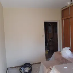 Pokój w Łasku po świeżym pomalowaniu ścian na jasny kolor, zabezpieczone meble folią, widoczny worek ze śmieciami po pracy.