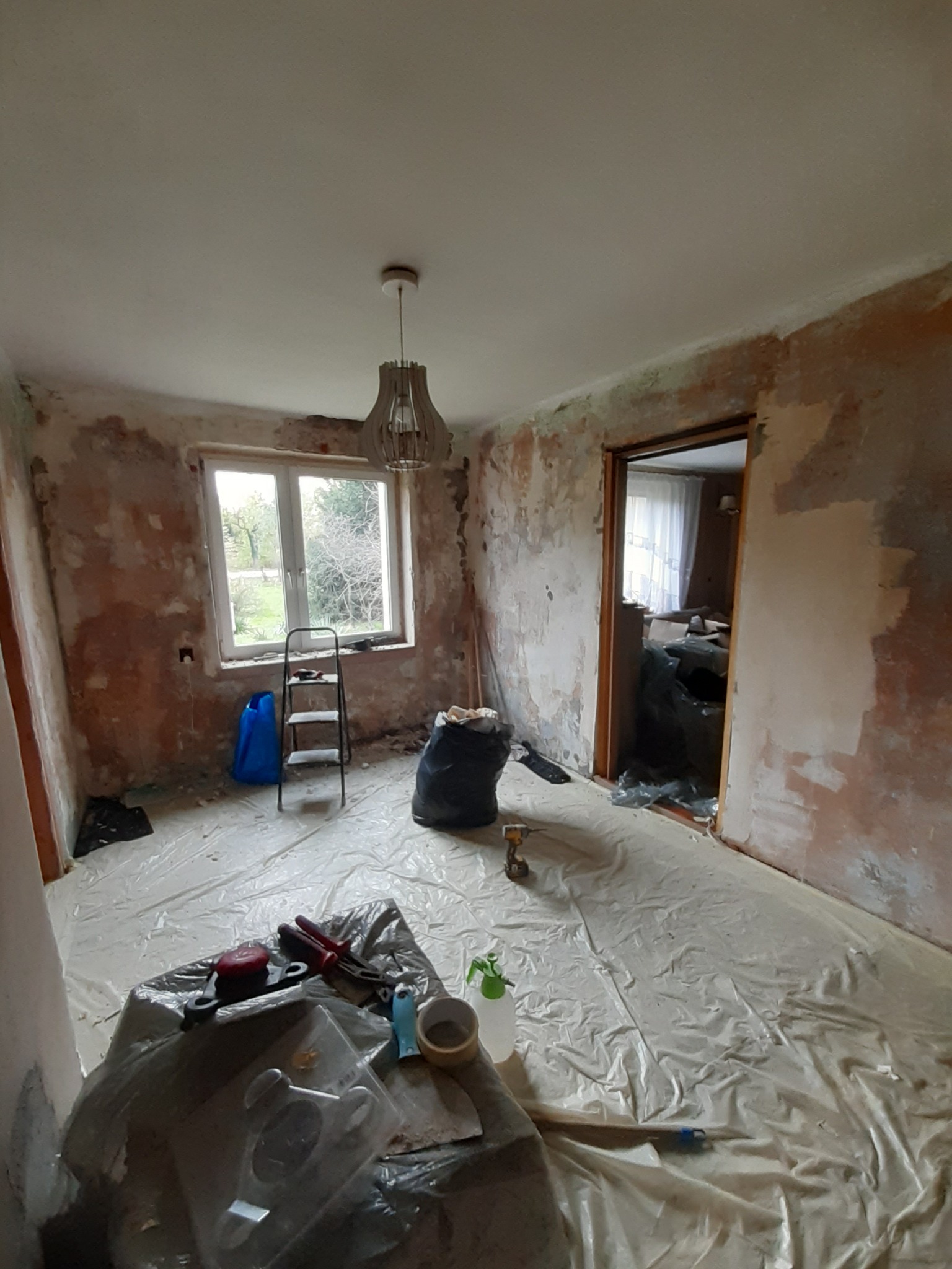 Pokój w Łasku przygotowywany do nałożenia gładzi: zabezpieczona folią podłoga, ściany częściowo pokryte masą, widoczne narzędzia i drabina.