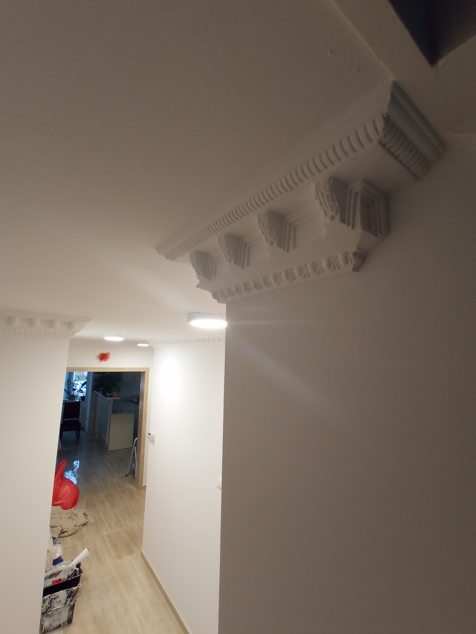 Białe, ozdobne listwy sufitowe zamontowane w korytarzu, widok na korytarz z elementami wyposażenia i narzędziami.