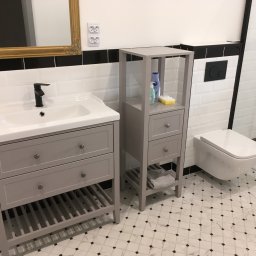 Dom - Art - Nowoczesna łazienka z szarą szafką pod umywalką, regałem i podwieszaną toaletą. Białe płytki z czarnym paskiem i wzorzysta podłoga.