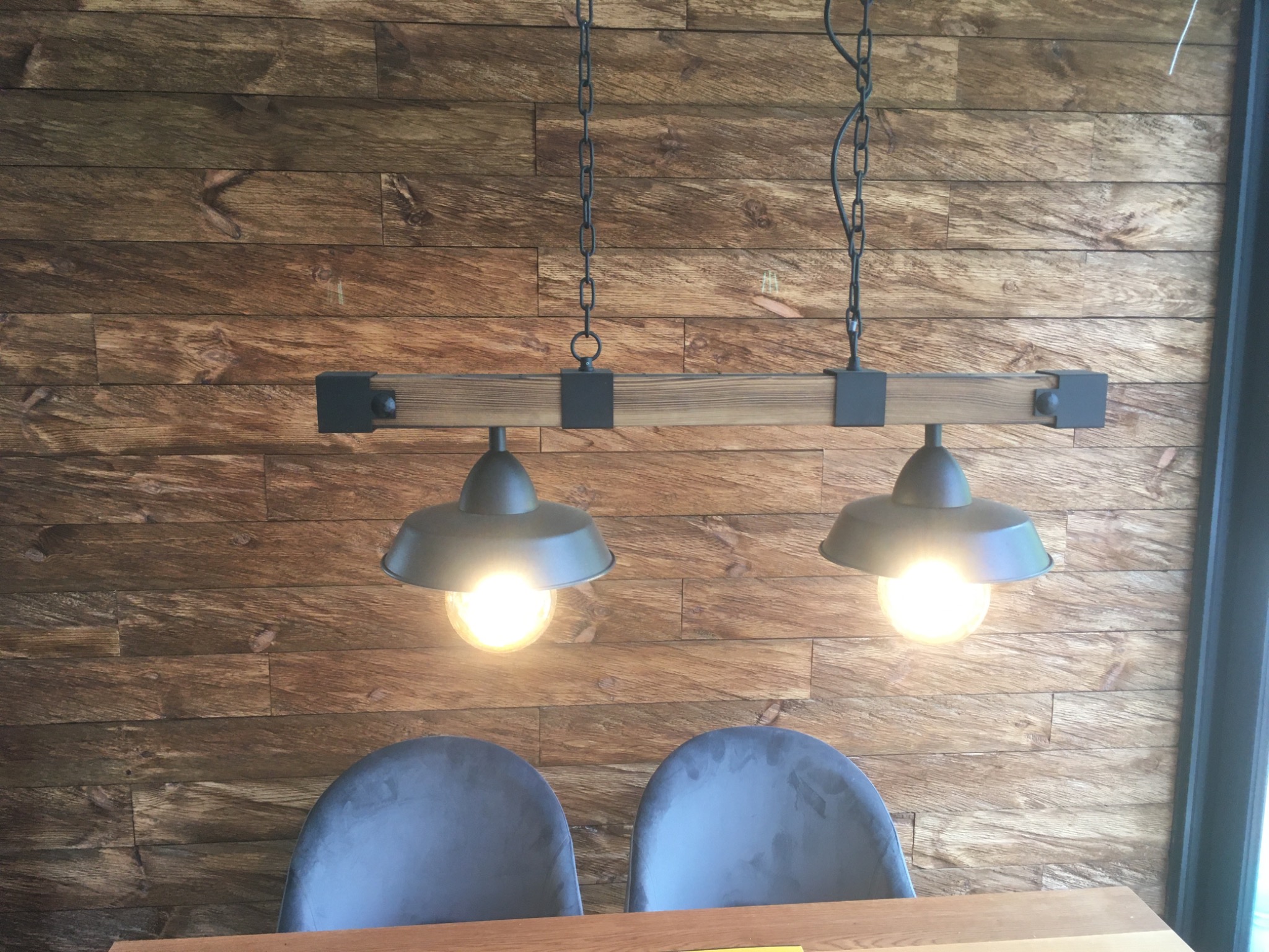 Drewniana ściana z dekoracyjną lampą wiszącą nad dwoma krzesłami. Industrialny styl oświetlenia i wykończenia wnętrza. Ciepłe światło żarówek.