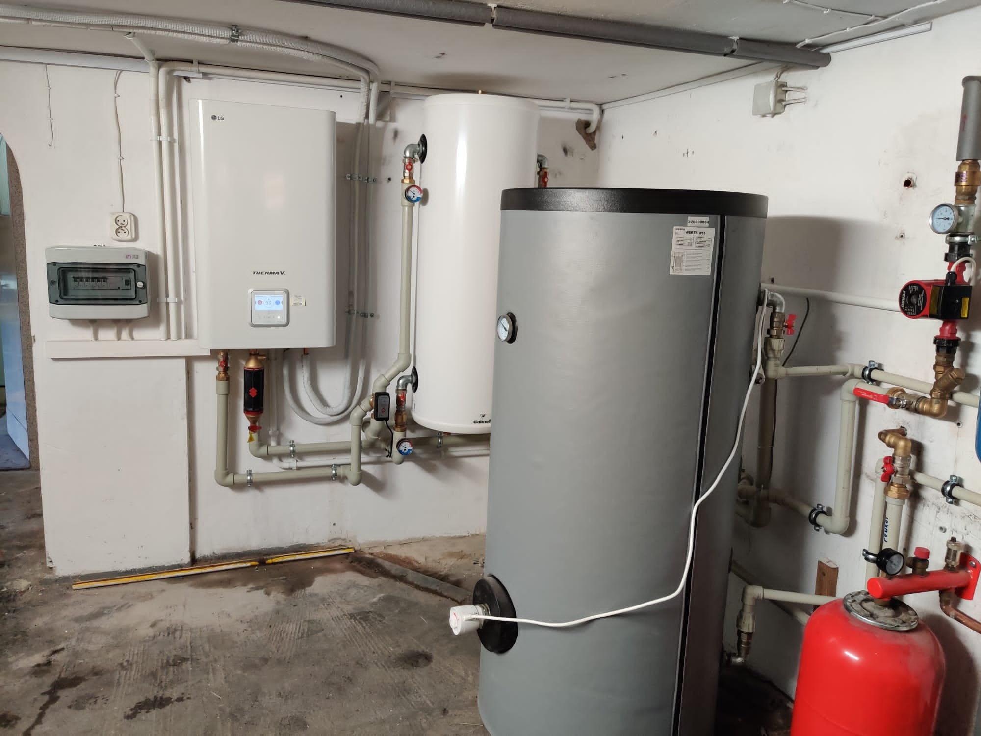 Instalacja pompy ciepła LG Therma V z zbiornikami Galmet i Webert W15 w piwnicy, widoczne rury, zawory i osprzęt, zasilanie elektryczne.