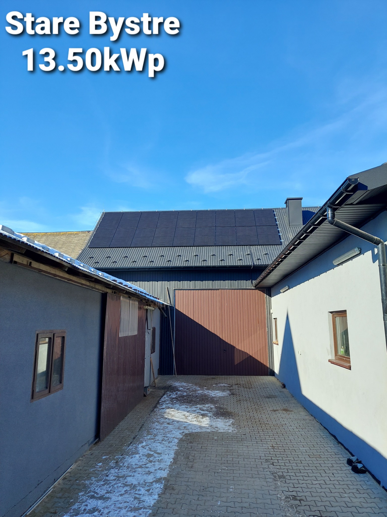 Instalacja paneli słonecznych o mocy 13.50kWp na dachu budynku gospodarczego w Starym Bystrym, widok z dołu na tle błękitnego nieba.