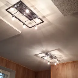 Wykończony sufit z zamontowanym oświetleniem punktowym, widoczne panele sufitowe i okna z folią ochronną.