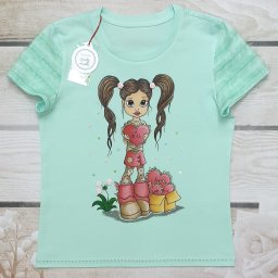 Pracownia Krawiecka CASSIE Jolanta Szymczak - Jasnomiętowa koszulka dziecięca z ręcznie malowaną dziewczynką trzymającą serce z napisem 'Kiss', obok pudełko z sercami, na drewnianym tle.