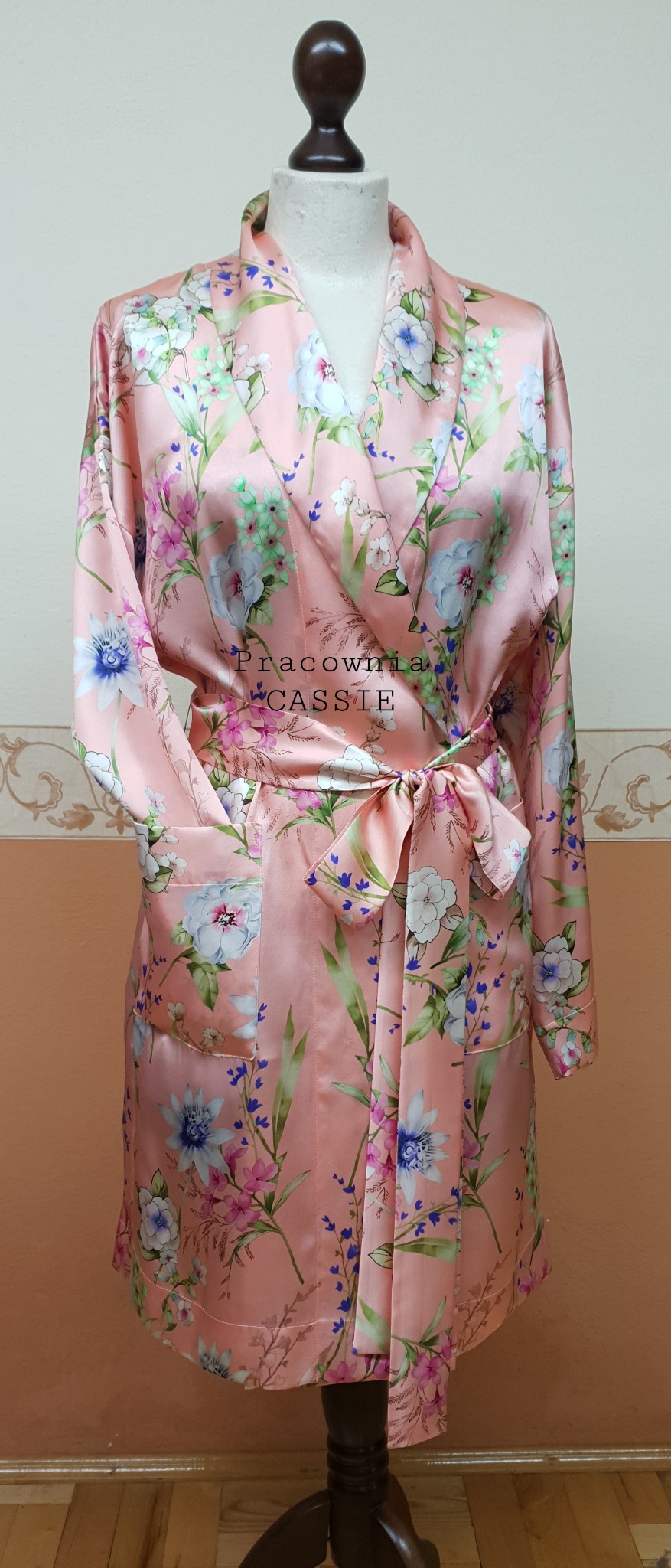 Satynowy, kwiecisty szlafrok damski w odcieniach różu i błękitu, zawiązany w pasie, prezentowany na manekinie.