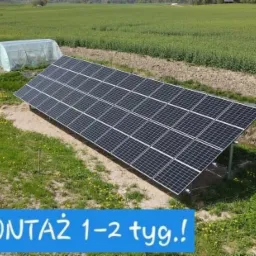 Panel słoneczny zamontowany na łące z widocznymi polami uprawnymi w tle, obok mały tunel foliowy. Na zdjęciu widoczny napis 'Montaż 1-2 tyg.'