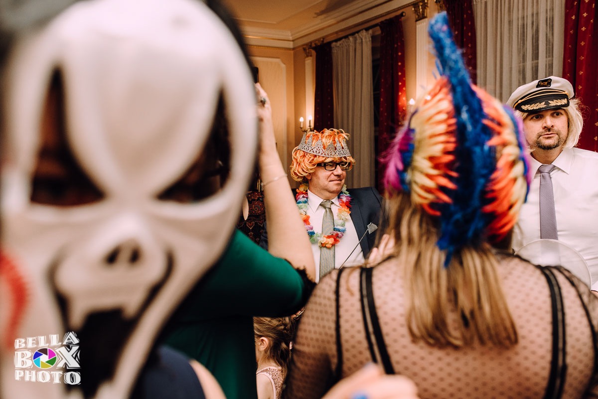 Osoby w przebraniach i maskach pozują w pomieszczeniu. W tle widoczne czerwone zasłony i dekoracje.