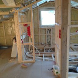 Kreative Home - Wnętrze w trakcie budowy, widoczne drewniane ramy ścian działowych, instalacje elektryczne z czerwonymi puszkami, rury instalacji wodnej i okno w dachu, podłoga w surowym stanie, częściowo...