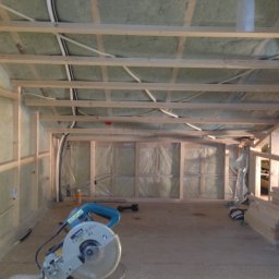 Kreative Home - Wnętrze w trakcie budowy: szkielet konstrukcji drewnianej, izolacja ścian, widoczne przewody i narzędzia, w tym piła tarczowa.