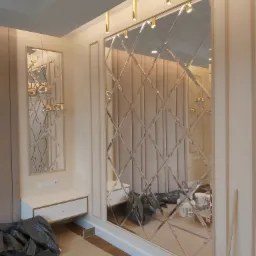 Dekoracyjne lustro ścienne z romboidalnymi elementami w kremowym wnętrzu, widoczne zabezpieczenia podłogi podczas montażu.