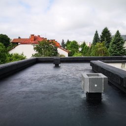 Forma Budownictwo Paweł Dąbrowski - Czarny, płaski dach pokryty papą termozgrzewalną z wystającymi elementami wentylacyjnymi z betonu komórkowego, widok na zabudowę jednorodzinną w tle.