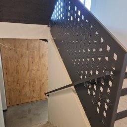 Forma Budownictwo Paweł Dąbrowski - Klatka schodowa w surowym stylu z betonowym sufitem, drewnianą zabudową i metalową ażurową balustradą z motywem rombów.