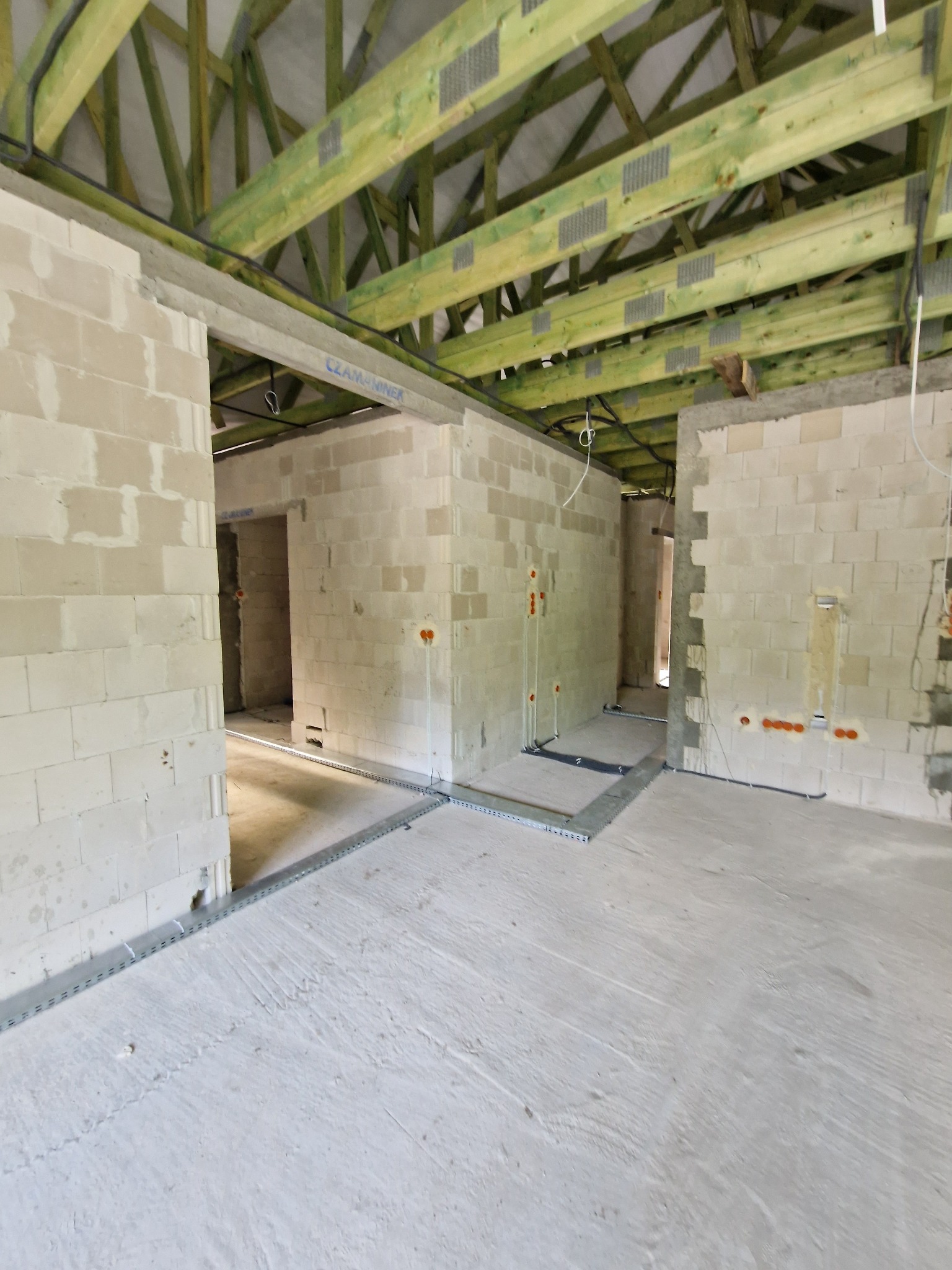 Wnętrze w trakcie budowy z surowymi ścianami z betonu komórkowego, widoczne instalacje elektryczne i podkonstrukcja dachu z impregnowanego drewna.