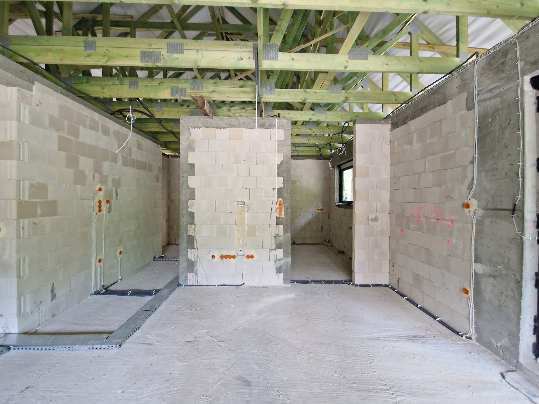 Wnętrze domu w stanie surowym otwartym z widocznymi ścianami z bloczków, drewnianą konstrukcją dachu, instalacją elektryczną w peszlach i korytkami kablowymi na podłodze.
