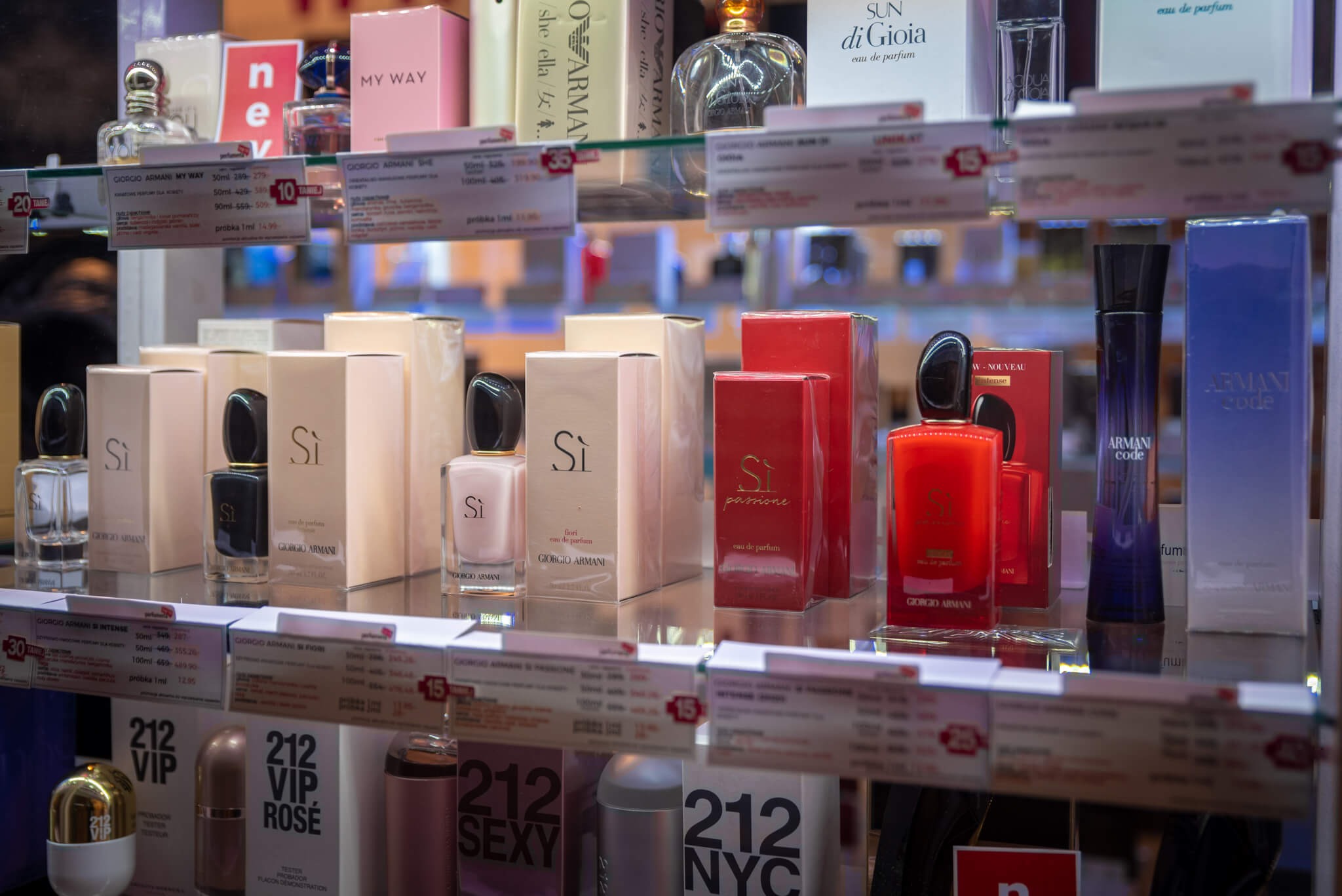 Półka w perfumerii z różnorodnymi flakonami i opakowaniami perfum Giorgio Armani, w tym serie Si, Si Passione, My Way i Armani Code, widoczne ceny promocyjne na etykietach.