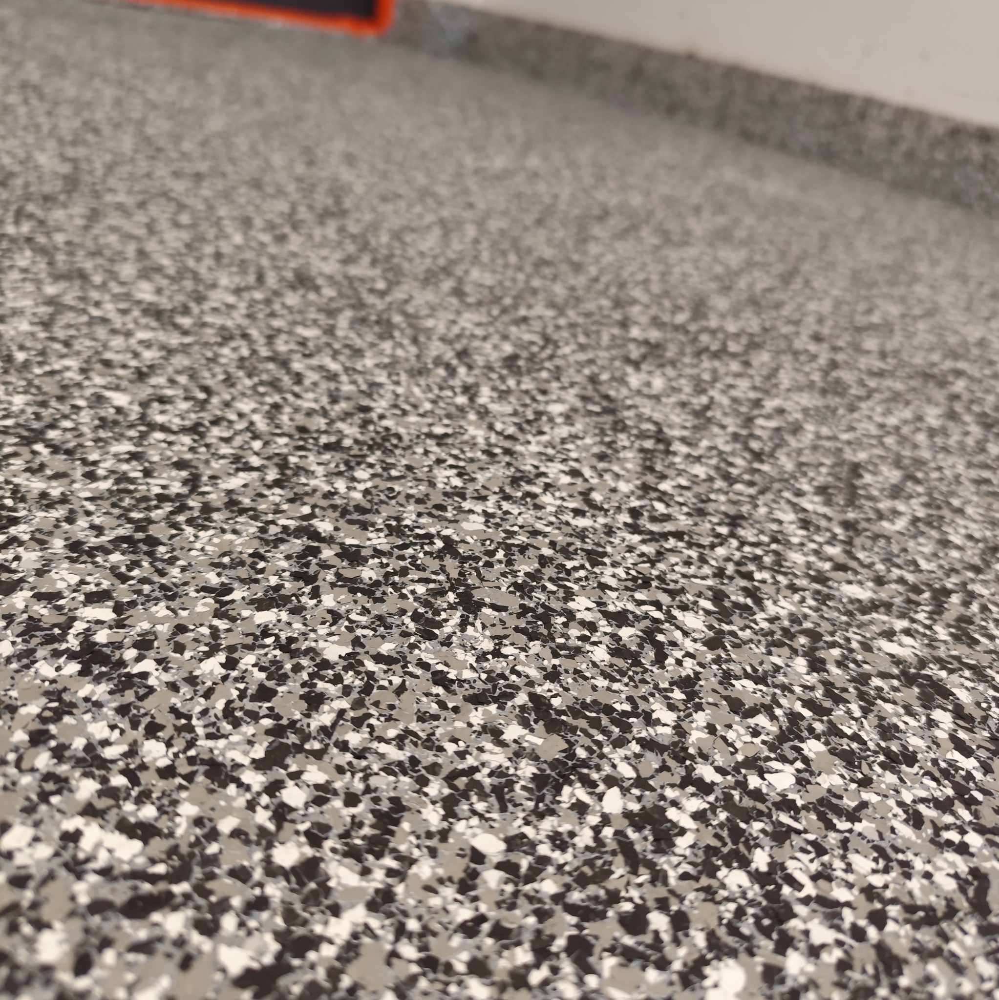 Szara posadzka z drobnymi, nieregularnymi plamkami w odcieniach bieli, szarości i czerni, widziana z niskiej perspektywy, ukazująca fakturę i wzór.