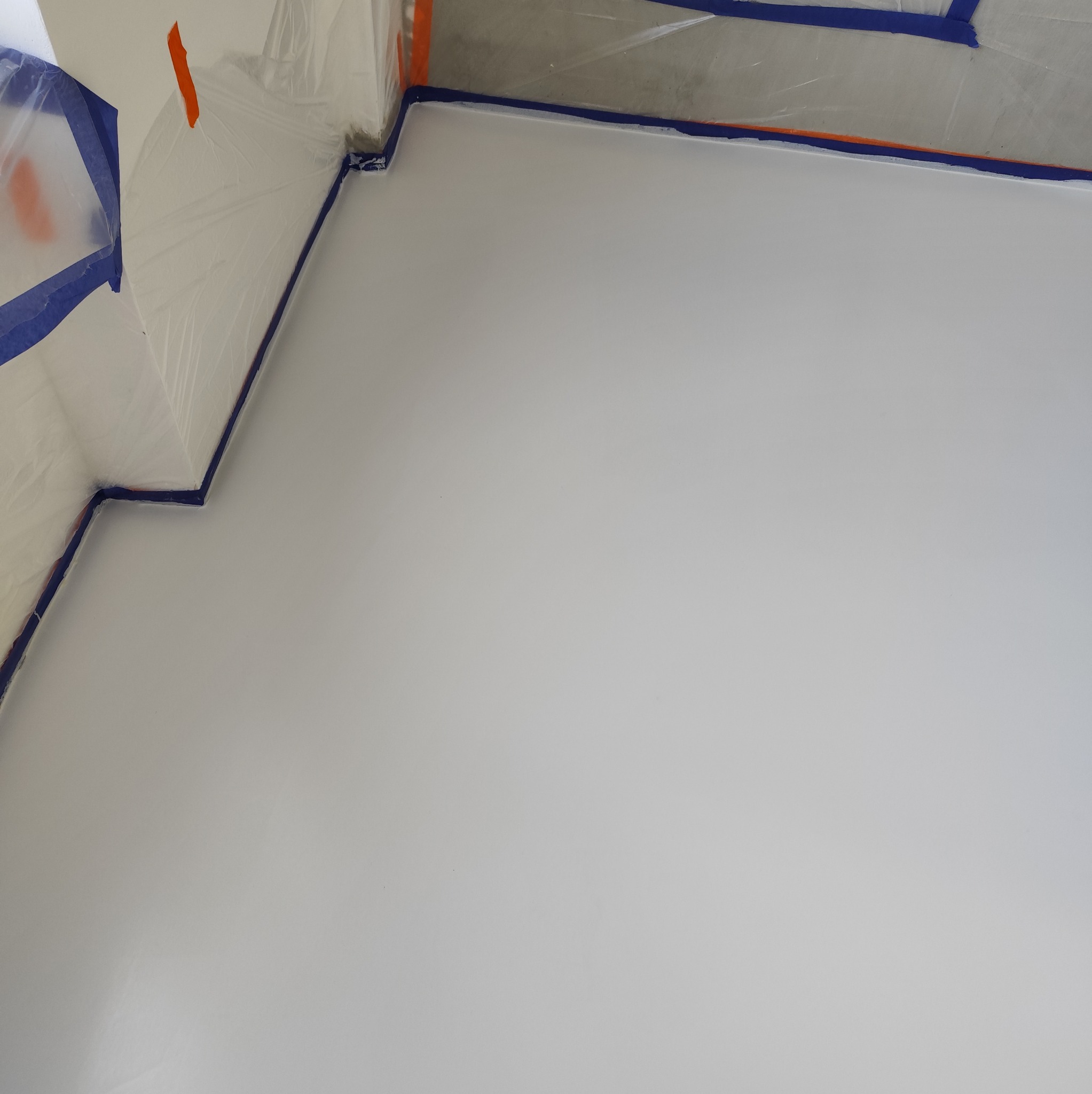 Świeżo wylana, jasnoszara podłoga w pomieszczeniu zabezpieczonym folią i taśmą malarską na ścianach i suficie.