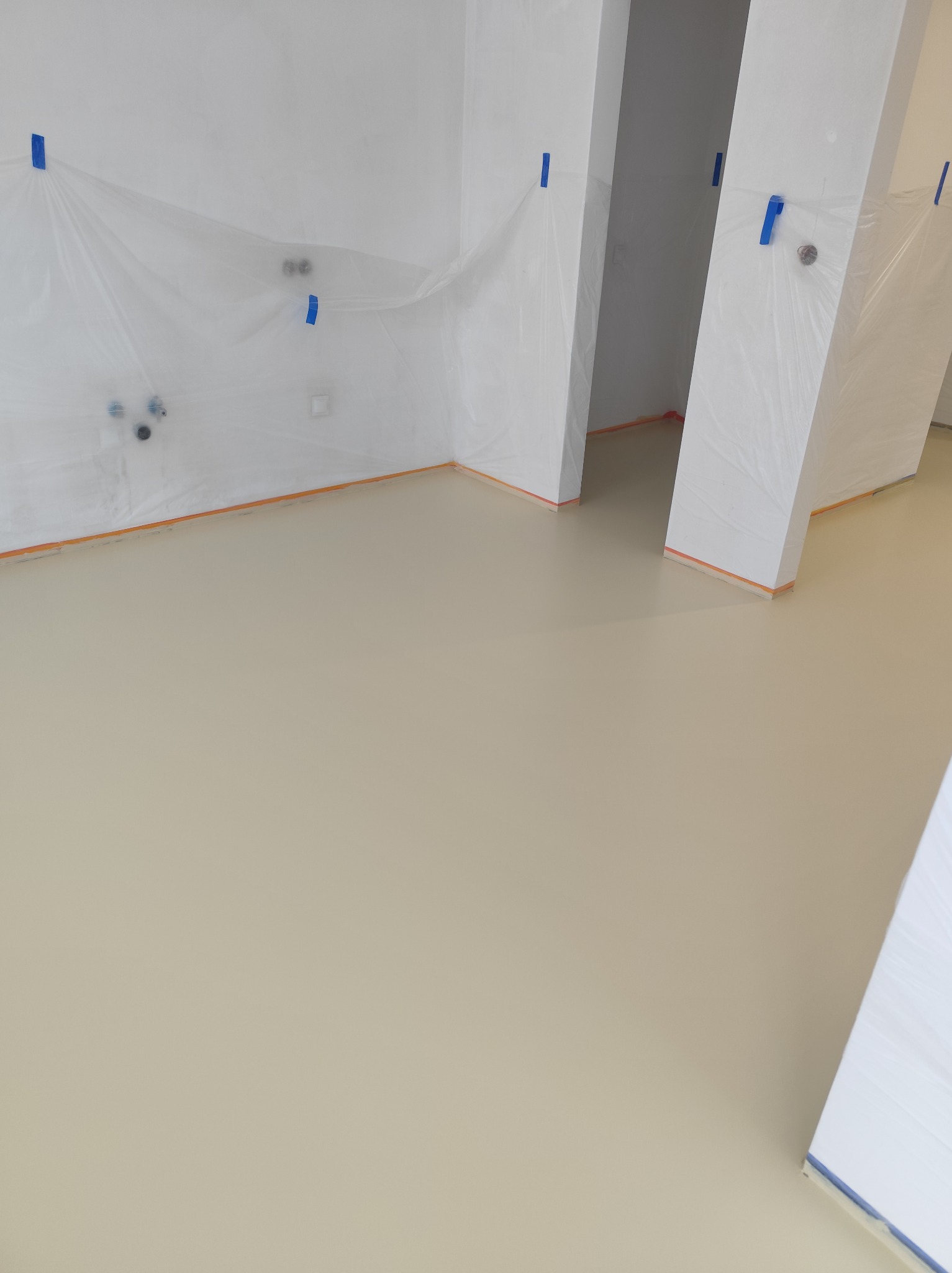 Jasna, gładka podłoga w nowym wnętrzu, zabezpieczone ściany folią i taśmą malarską. Minimalistyczny design, świeżo wylana powierzchnia. Widok z góry.